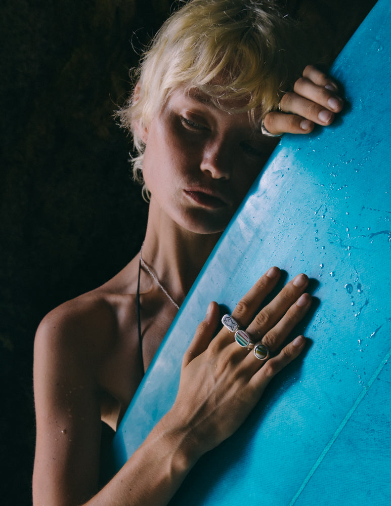 A close-up of hands resting on a vibrant blue surfboard, showcasing rings and droplets of water on the board's surface.