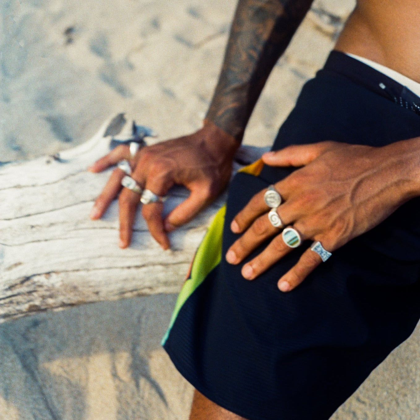 A close-up of a man’s hands resting on a log, showcasing multiple silver rings.