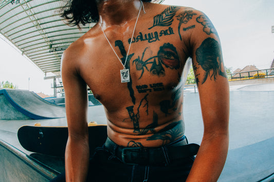 Male Skateboarder Wearing Black Cat Dog Tag Pendant Necklace at Skatepark with Skateboard in Background