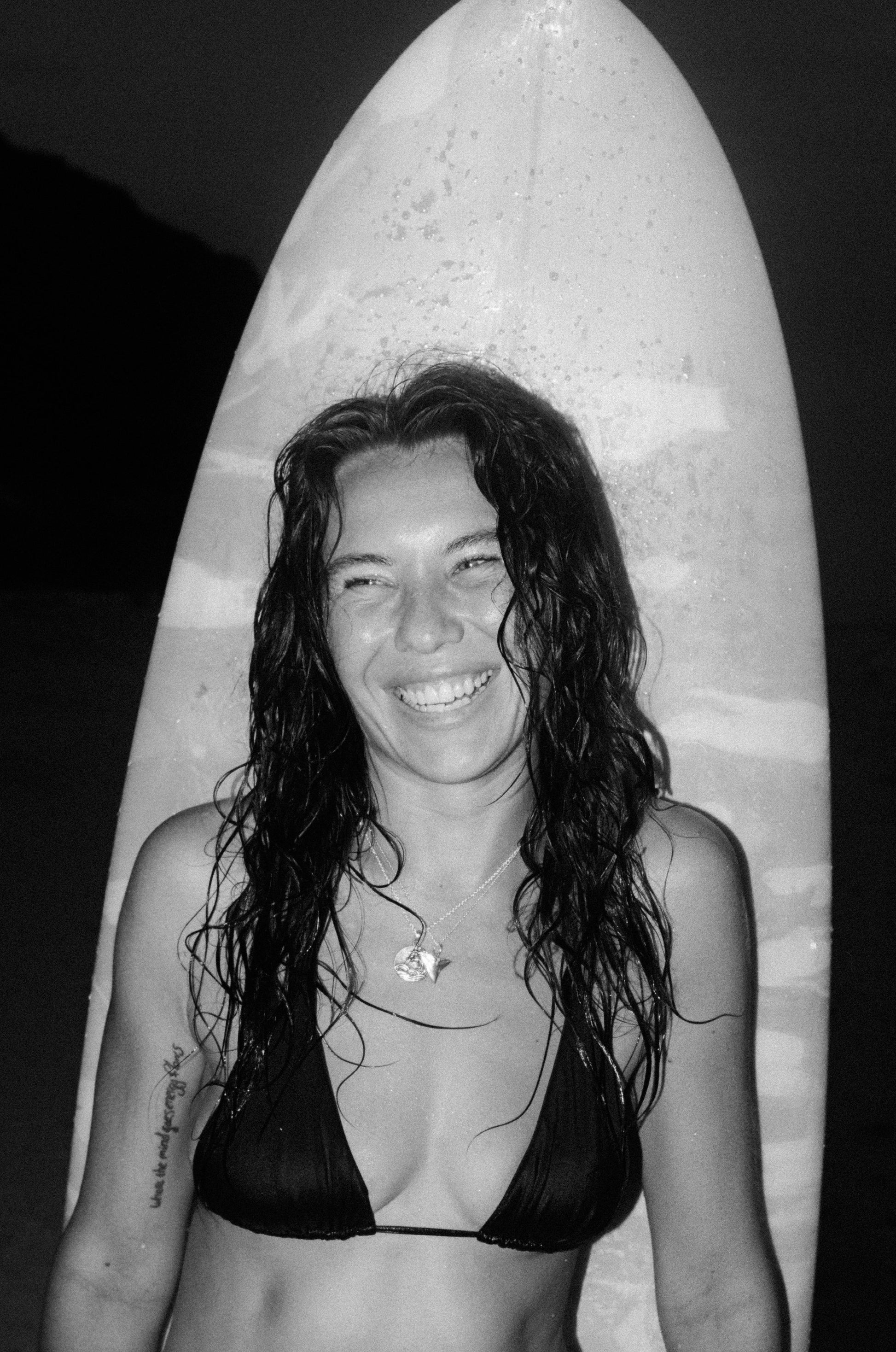 Black and white photo of Model smiling with Shark Tooth Pendant necklace on infront of surfboard 