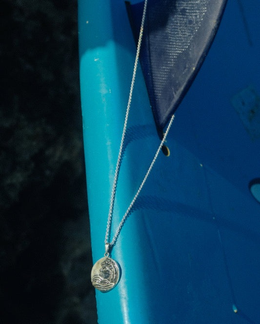 Lifestyle shot of Sterling Silver Handmade Tsunami Pendant Necklace hung on Surfboard Fin in a Surfboard.